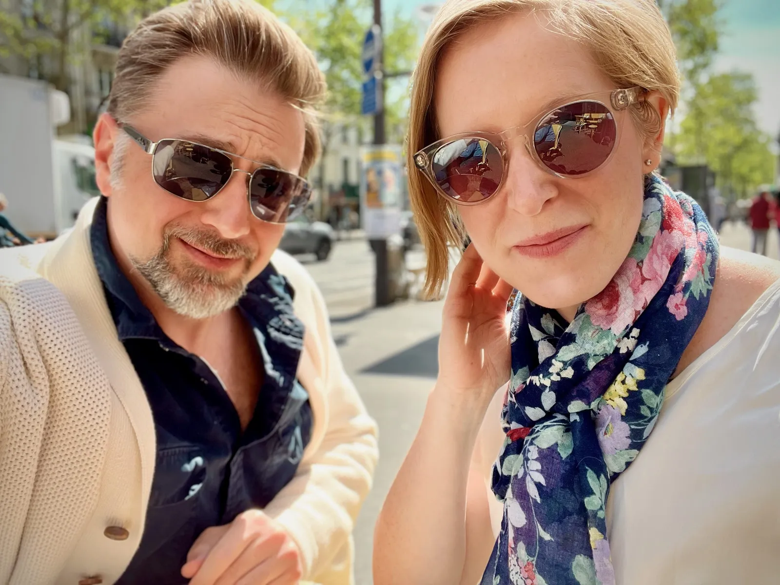 A close up of a couple wearing sunglasses outdoors on a city street.