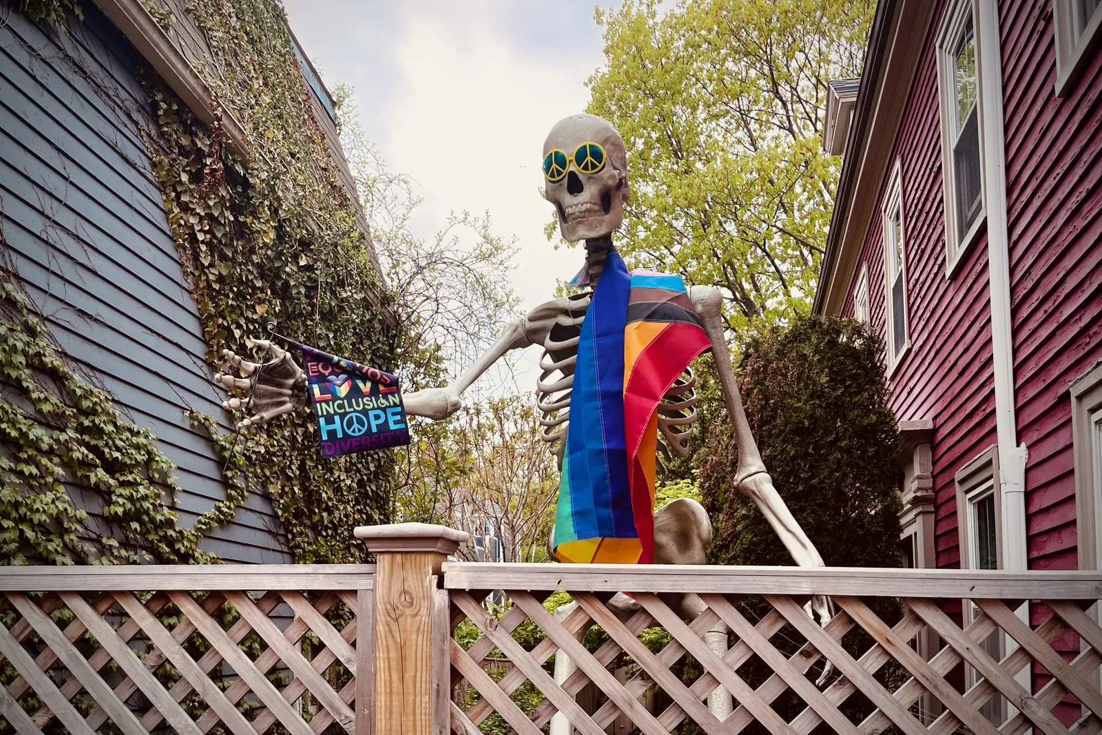 A 12 foot skeleton, draped in a rainbow flag, peace glasses, and holding a flag that celebrating inclusion, hope, and diversity.