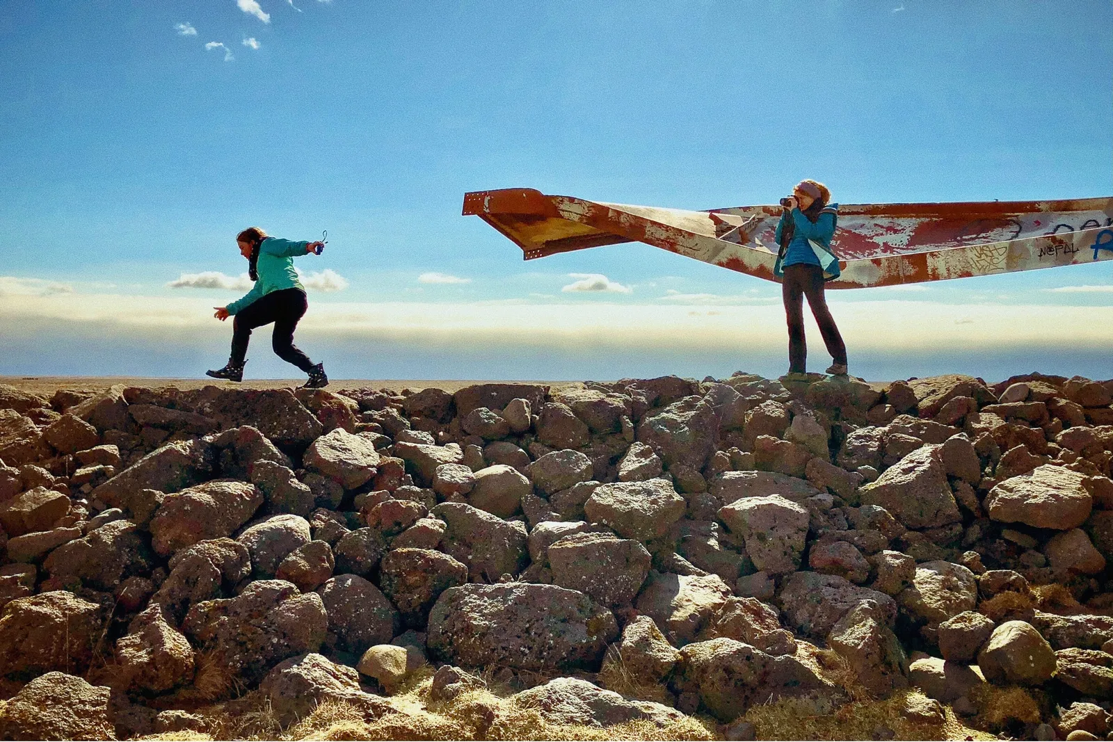 Two people standing on a rock pile. There is a steel beam suspended horizontally behind one.